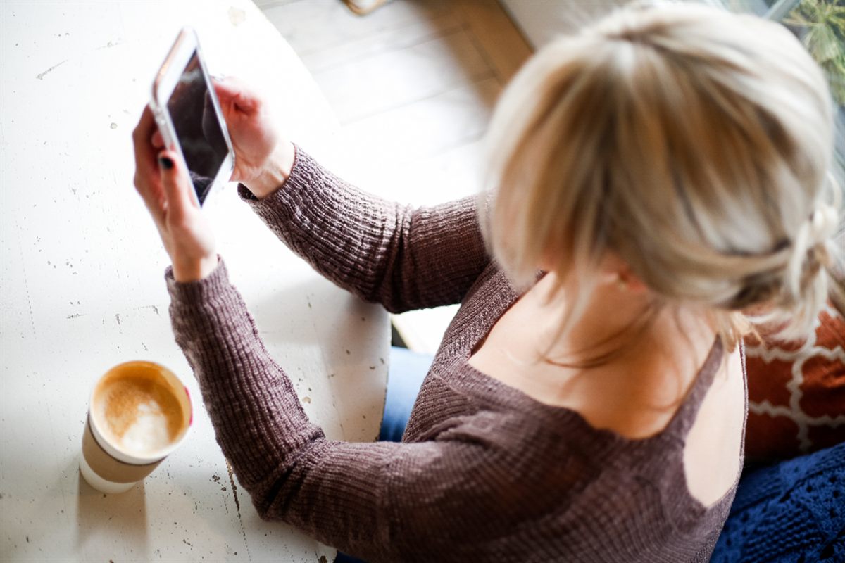 Mujer mandando una nota de voz desde el móvil con un café al lado